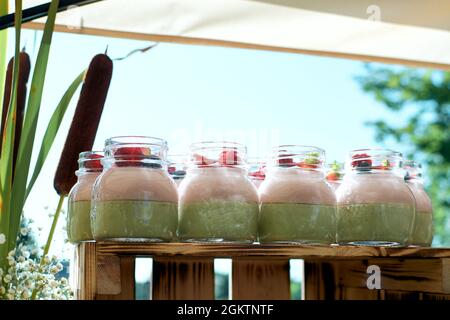 Cremige Desserts in Gläsern. Desserts mit frischen Beeren dekoriert. Fragment der festlichen Tafel. Einrichtung von Reed. Stockfoto