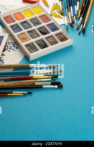 Aquarellfarben und Pinsel. Arbeitsplatz und Schreibtisch des Künstlers. Farbpalette. Blauer Hintergrund wird gezeichnet. Ort für Ihren Text. Kunst erstellt. Speicherplatz kopieren Stockfoto