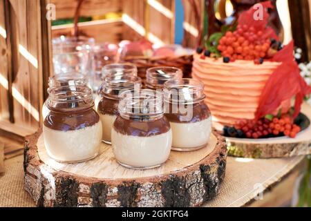 Schokoladencreme-Dessert in einem Glas. Desserts stehen auf einem Holzblock, mit einem Geburtstagskuchen im Hintergrund. Fragment eines süßen Tisches in einem Rusti Stockfoto