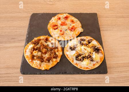 Verkostung von spanischen Pizzas mit Pilzen, Blutwurst, Käse, serrano-Schinken, Zwiebeln, Huhn und Pinienkerne auf einem schwarzen Schieferteller Stockfoto