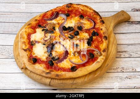 Typische italienische Pizza mit roten Zwiebeln, schwarzen Oliven, Thunfisch aus der Dose, Mozzarella-Käse und Pomodoro auf Holzbrett Stockfoto