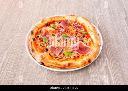 Kleine Pizza mit serrano-Schinken, schwarzen Oliven, Basilikumblättern, Pilzscheiben und Mozzarella-Käse Stockfoto