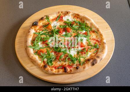 Weizenmehl-Pizza mit Burrata-Käse, gerösteten Kirschtomaten und Rucola auf grauem Hintergrund Stockfoto