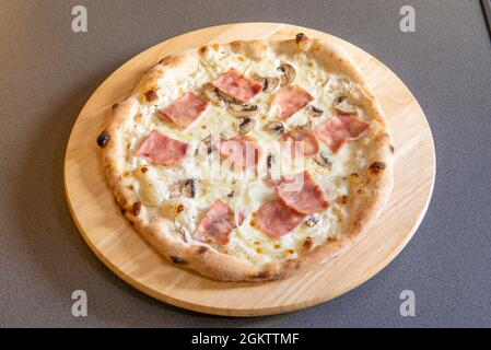 Kleine Pizza mit Zutaten aus Carbonara-Sauce, Speck, Bechamel, Pilzen und Zwiebeln auf Holzbrett Stockfoto