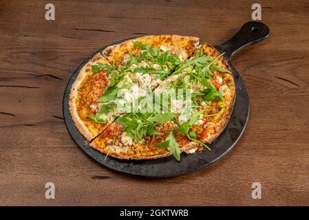 Pizza mit viel Feta-Käse und Rucola und mit orientalischem Touch im türkischen Mehlteig auf schwarzem Teller Stockfoto