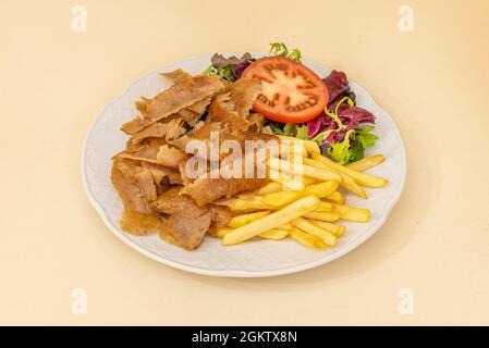 Döner-Teller mit gewürzten Lammscheiben, Bratkartoffeln und Eichensalat sowie Tomatenscheiben in einem Restaurant Döner-Döner auf weißem Teller Stockfoto