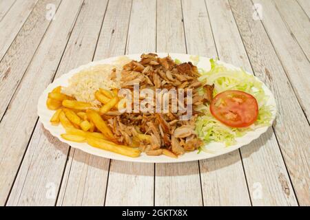 Kebab-Menütablett mit pommes frites, Basmati-Reis, gehacktem, gebratenem Hähnchenfleisch, Zwiebeln und Eisbergsalat mit Tomate auf weißem Tisch. Stockfoto