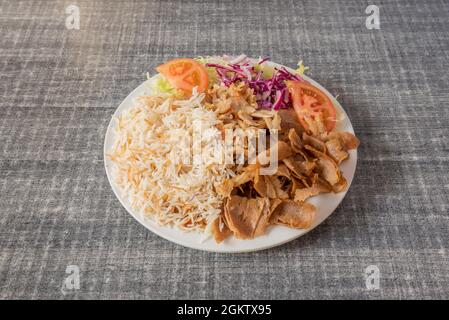 Beliebte gemischte Kebab-Gericht aus Lammfleisch und Hühnerfleisch mit Basmati-Reis-Guarnicion, Krautsalat, gehackten Tomaten und Eisbergsalat auf grauem Tisch Stockfoto