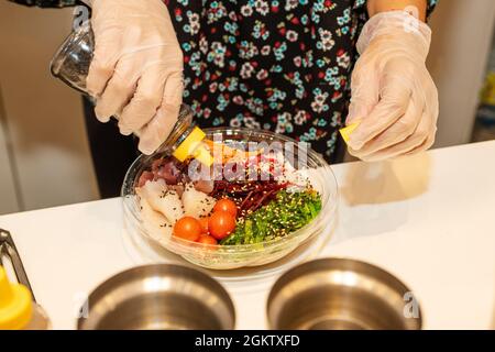 Kochen Sie Tuna Poke Bowl Dressing und geräucherter Poppet mit Kirschtomaten, Rüben und Wakame Seetang Salat in klarem Kunststoff nach Hause Lieferbehälter. Stockfoto