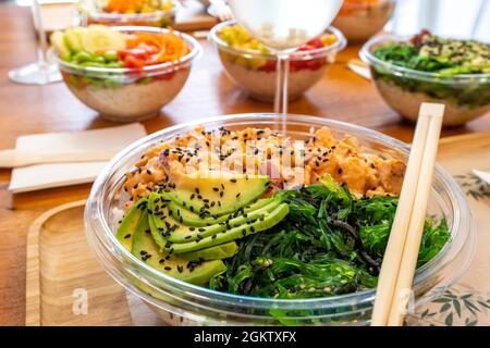 Marinierte Hähnchenschüssel mit Avocado-Scheiben, Wakame-Algen, Sauce, Mohn, Zahnstochern und Bambusblech Stockfoto