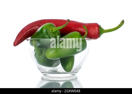 Eine Schote scharfem Rot und mehrere Schoten grünen Pfeffers in einer Glasschüssel, Nahaufnahme, isoliert auf Weiß. Stockfoto