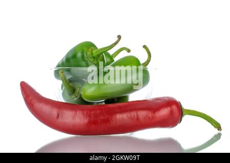 Eine Schote scharfem Rot und mehrere Schoten grünen Pfeffers in einer Glasschüssel, Nahaufnahme, isoliert auf Weiß. Stockfoto