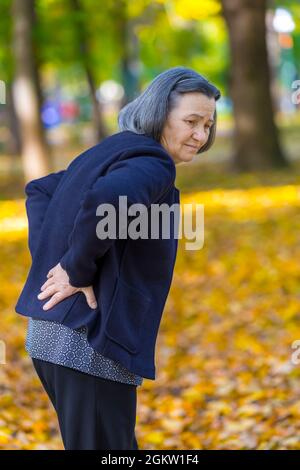 Ältere Frau, die im Herbstpark unter Rückenschmerzen leidet. Stockfoto