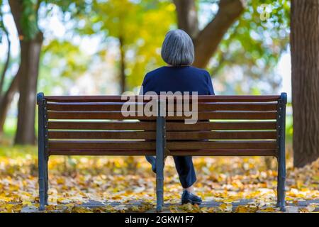 Ältere Frau, die im Herbstpark auf der Bank sitzt. Stockfoto