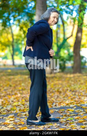 Ältere Frau, die im Herbstpark unter Rückenschmerzen leidet. Stockfoto