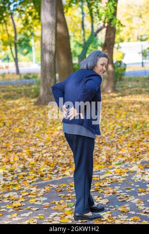 Ältere Frau, die im Herbstpark unter Rückenschmerzen leidet. Stockfoto