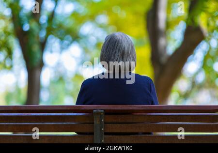 Ältere Frau, die im Herbstpark auf der Bank sitzt. Stockfoto