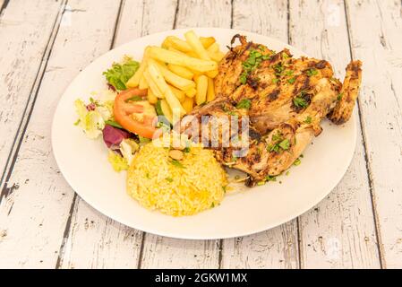 Vollkohle-Hähnchenmenü mit asiatischem Reis, Pommes frites, Salat und Tomatensalat, Petersilie und Mandeln auf einem runden Teller Stockfoto