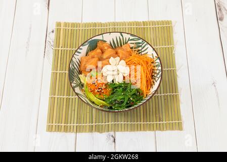 Poke eine Schüssel in einem super coolen Behälter auf einem Bambusgestell mit Fischrogen, mariniertem Lachs, vielen geriebenen Karotten, gerollten Avocado, Wakame-Algensalat und Stockfoto