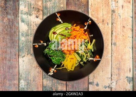 Hawaiianische marinierte Lachsschüssel, reife Avocado-Scheiben, geriebene Paprika und Karotten, Wakame-Algensalat und geriebene Zucchini in einer schwarzen Schüssel Stockfoto