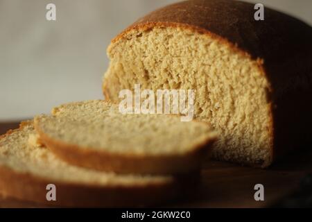 Scheiben selbstgebackenes Weizenbrot, auf einem Holzbrett gehalten. Stockfoto