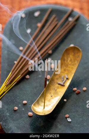 Selektiver Fokus von Weihrauch auf einer Steintafel und Räucherstäbchen auf der Seite, orangefarbenem Stoffhintergrund und Rauch im Vordergrund Stockfoto