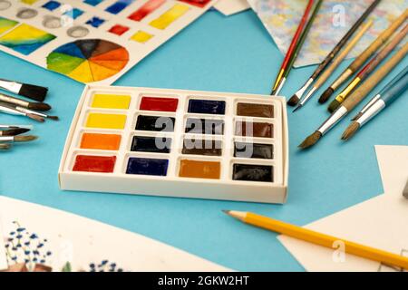 Eine Schachtel Aquarelle mit Pinsel. Zeichnen, Hintergrund. Verpackung von bunten neuen Farben auf dem Tisch. Putzen und malen. Zeichnen und Hobbie. Stockfoto