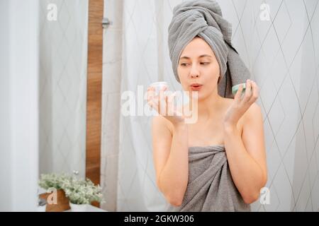 Frau im Badezimmer hält ein Glas feuchtigkeitsspendende Creme für Gesicht und Körper. Stockfoto