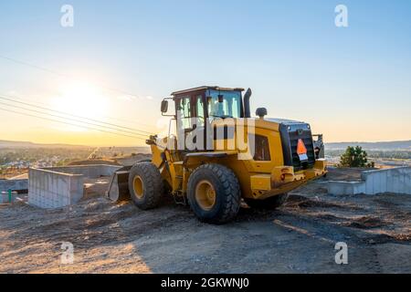 Ein Traktor, der bereit ist, Schmutz zu bewegen und auf einer neuen Baustelle auf einem Hügel mit Blick auf die Stadt Spokane, Washington, USA, in der Nähe des Sonnenuntergangs auszugraben. Stockfoto