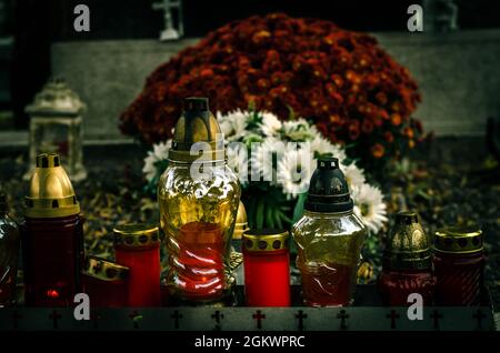 Brennende Kerzen, Chrysantheme-Blumen und Begräbnisdekorationen auf Gräbern auf dem Friedhof Stockfoto