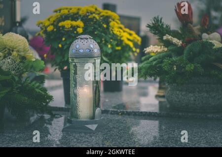 Brennende Kerzen, Chrysantheme-Blumen, Symbole und andere Verzierungen auf Gräbern auf dem Friedhof während Allerheiligen Stockfoto