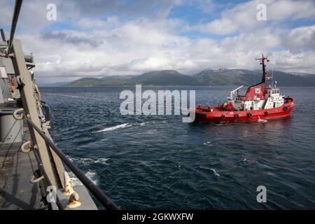 TROMSO, Norwegen (14. Juli 2021) Ein Schlepper unterstützt den Arleigh-Burke-Klasse-Lenkflugkörper-Zerstörer USS Roosevelt (DDG 80) beim Abflug von Tromso, Norwegen, 14. Juli 2021. Roosevelt, der im spanischen Rota stationiert ist, befindet sich auf seiner zweiten Patrouille im Einsatzgebiet der Sechsten US-Flotte zur Unterstützung regionaler Verbündete und Partner sowie der nationalen Sicherheitsinteressen der USA in Europa und Afrika. Stockfoto