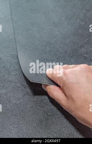Verschiedene Böden. Renovierungs- oder Baukonzept. Nahaufnahme einer männlichen Hand, die eine strukturierte Bodenplatte aus Vinyl hält. Proben von Laminat und Vinyl Stockfoto