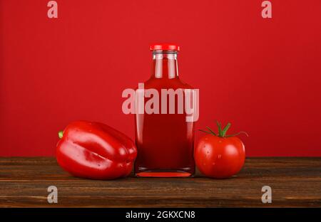 Nahaufnahme einer Glasflasche Ketchup-Sauce, frischen Tomaten und Paprika auf einem Holztisch auf rotem Hintergrund mit Kopierraum und tiefer Sicht Stockfoto