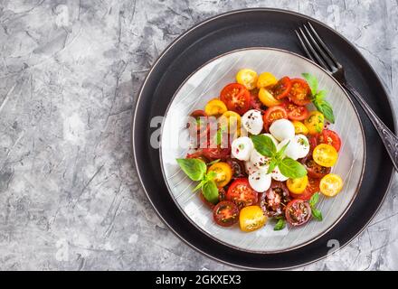 Frischer Salat aus roten und gelben Kirschtomaten mit Baby-Mozzarella-Käse und Basilikum, Nahaufnahme Stockfoto