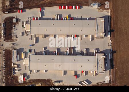 LKW mit Anhänger warten im Verladerager auf die Verladung von Waren für den Transport. Luftaufnahme von oben. Ein großer Transitfrachtterminal mit Parkplätzen, Lastwagen und Anhängern. Stockfoto