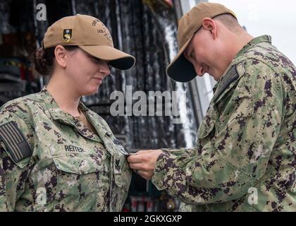 210719-N-WU807-1007 PHILIPPINE SEA (19. Juli 2021) Hospital Corpsman 1st Class Erica Reiter, links, aus North Smithfield, R.I., erhält die angeführte Air Warfare Specialist-PIN von Aviation Electrician's Mate 1st Class Alex Sidwell, aus Los Angeles, angebracht an Helicopter Sea Combat Squadron (HSC) 21, Zugewiesen an Independence-Variant Littoral Combat Ship USS Charleston (LCS 18), Juli 19. Charleston, Teil von Destroyer Squadron Seven, befindet sich im Rotationseinsatz und ist im Einsatzgebiet der 7. US-Flotte tätig, um die Interoperabilität mit Partnern zu verbessern und als einsatzbereite Truppe i zu dienen Stockfoto