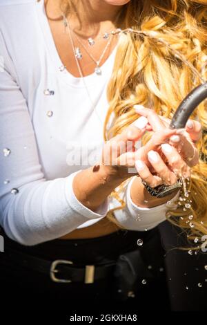 Kaukasisches Mädchen mit blondem lockiges Haar trinkt Wasser aus einem historischen traditionellen Trinkbrunnen im Freien in Rom. Heißer Sommertag. Lässiger Style Stockfoto