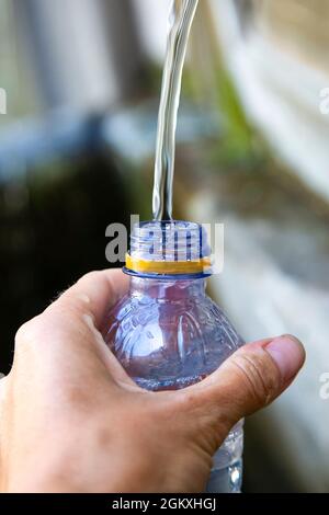 kaukasische Frauenhand mit blu-Plastikflasche. Mädchen füllt eine Flasche mit frischem reinem Wasser an einem Sommertag. Trinkwasser im Freien Brunnen. Wasser Stockfoto