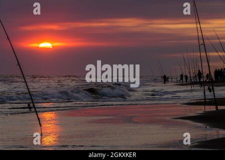 Fischer mit ihren Angelruten bereit, bei einem Sonnenuntergang an der Küste zu fischen. Stockfoto