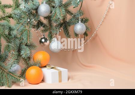 Weihnachten. Eine Neujahrskomposition aus Zweigen eines Weihnachtsbaums, verziert mit silbernen Kugeln, einer Geschenkbox, orange auf einem Hintergrund mit Fleisch-Co Stockfoto