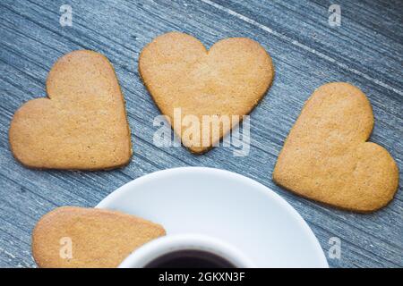 Drei Lebkuchen herzförmige Kekse in der Nähe der Grenze von weißem Porzellan Kaffeetasse. Kaffeepause mit Liebe. Hausgemachte Süßigkeiten. Momente der Zärtlichkeit Stockfoto