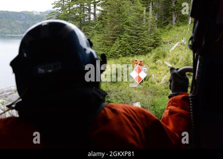 Ein Mitglied der Küstenwache der Flugstation Sitka beobachtet zwei Küstenwache-Aids für das Navigations-Team Sitka-Mitarbeiter, die Wartungsarbeiten an ATON in Sitka, Alaska, durchführen, 21. Juli 2021. Wenn Besatzungen auf ATON in abgelegenen Gebieten Alaskas arbeiten, werden Hubschrauber häufig eingesetzt, um die Besatzung und Ausrüstung dorthin zu bringen. Stockfoto