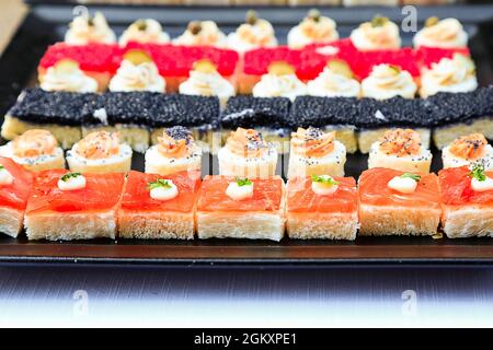 Viele kleine bunte Sandwiches mit Fisch, rotem und schwarzem Kaviar. Fingerfood mit Meeresfrüchten. Sushi wie kleine Snacks für die Hochzeit. Hintergrund. Menübild Stockfoto