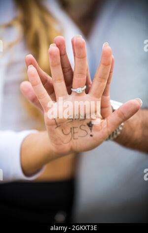 Ich sage ja. Worte, die auf die Hand der Frau geschrieben sind, mit Ehering und mans-Hand dahinter. Stockfoto