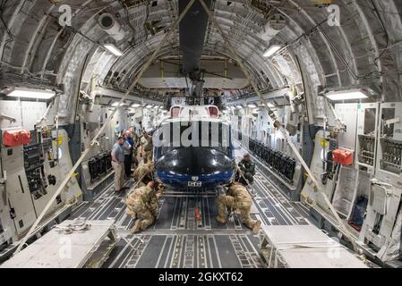 Flieger mit der 167. Operations Group und Helikopter-Betreuer mit Amentum überprüfen während eines Helikopter-Ladetrainings auf der Fluglinie bei Joint Base Andrews, Maryland, die Verzurrpunkte nach dem Laden des Huey-Hubschraubers UH-1N vom 1. Helicopter Squadron auf ein C-17 Globemaster III-Flugzeug mit dem 167. Airlift Wing, 21. Juli 2021. Das Training verbesserte die Effizienz und Effektivität des Ladens und Transportes dieser Hubschraubertypen. Stockfoto