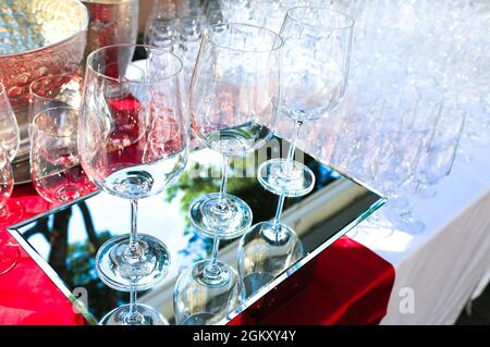 Drei Kristallweingläser auf verspiegelter Oberfläche mit vielen Gläsern dahinter. Catering-Service. Weinprobe Vorbereitung. Wichtige Party. Utensilien für Stockfoto