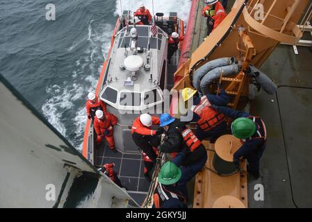 Die Crew-Mitglieder der Küstenwache Cutter Healy unterstützen die Crew-Mitglieder der Küstenwache Cutter Midgett, während sie vom Cutter-Boot in der Beringstraße an Bord klettern, 25. Juli 2021. Das Midgett ist ein nationaler Sicherheitsdienst, der die Präsenz der USA sicherstellt, um die Souveränität der USA und die Ressourcensicherheit in abgelegenen pazifischen Regionen zu gewährleisten. Stockfoto