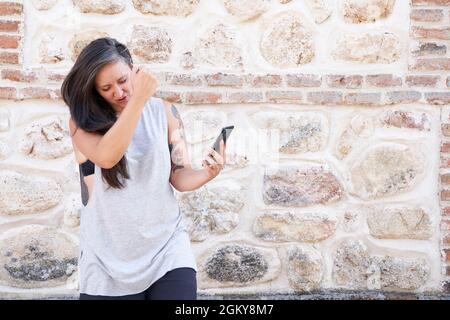 Aufgeregt und glücklich Frau, die auf den Telefonbildschirm schaut, einen Sieg mit Freude feiert und ihr Smartphone hält. Technologie- und Lifestyle-Konzept Stockfoto