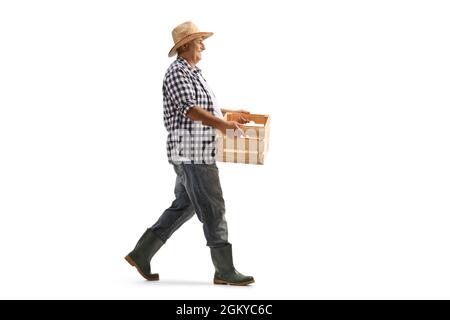Ganzkörperaufnahme eines reifen Bauern, der eine Kiste trägt und isoliert auf weißem Hintergrund läuft Stockfoto